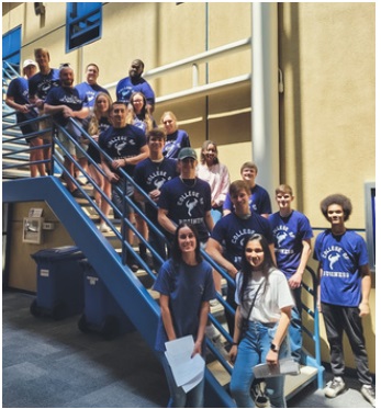 A group of future students all wearing their College of Business t-shirt on the steps of the College of Business lobby.