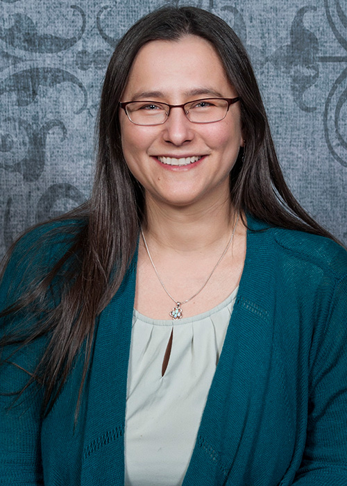 Headshot of woman with long hair in green top against light blue background.