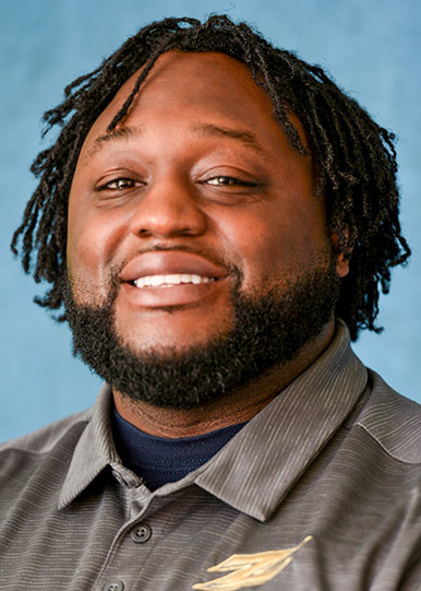 Photo of man in gray top smiling against blue background.