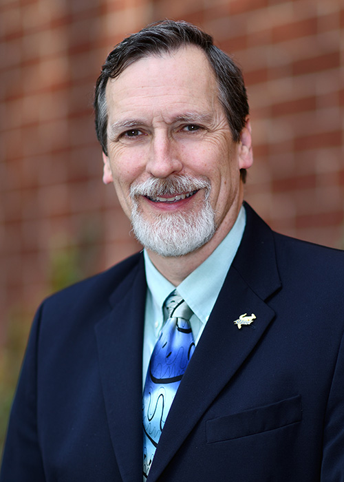 Photo of man in suit against brick background.